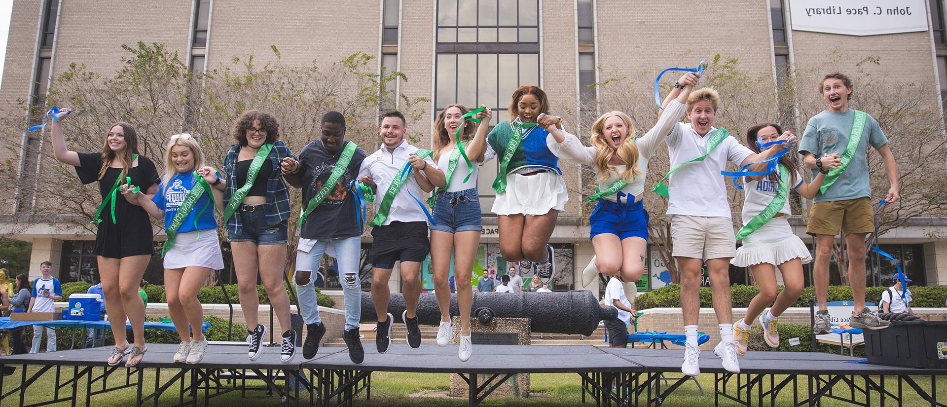 Students with Homecoming Court sashes jump in unison on Cannon Green